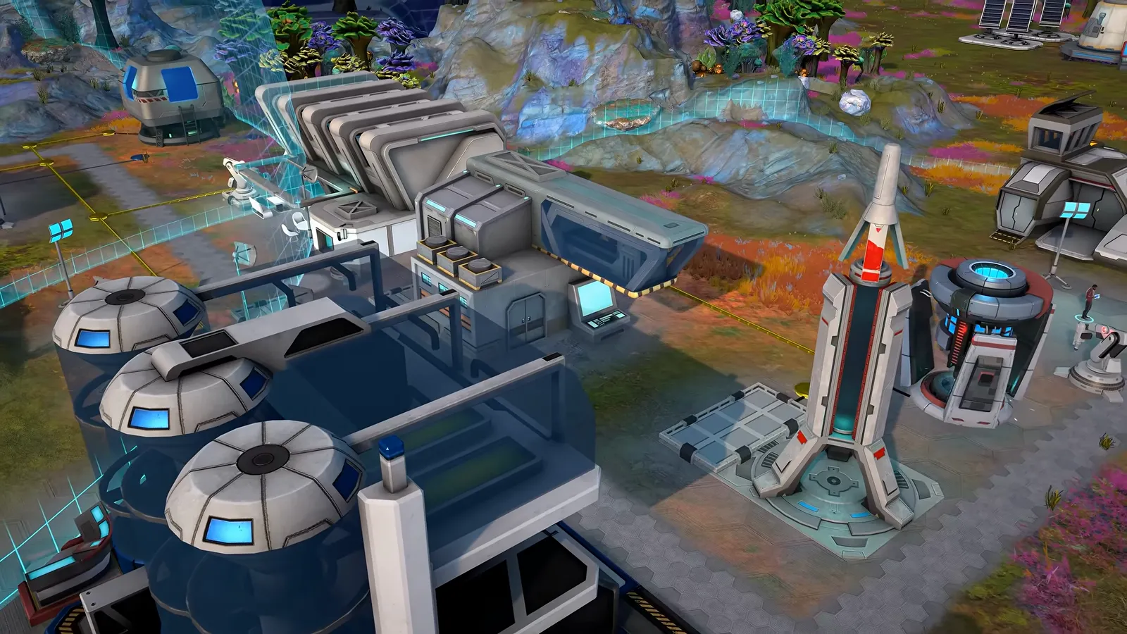 Official gameplay footage of an early outpost with grouped industrial modules, round tanks and a tall rocket-shaped structure on the hex grid